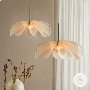 May include: Two pendant lights with petal-shaped shades in a soft, neutral color. The shades are made of a translucent material, and each light has a single bulb. The lights hang from thin, dark metal rods.