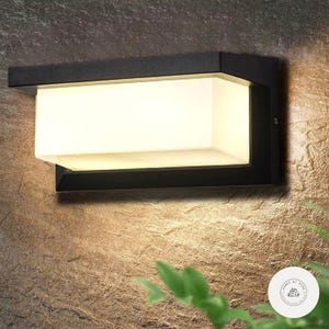 Puede incluir: Una lámpara de pared exterior rectangular negra con una luz blanca brillante. La luz está montada en una pared de piedra marrón texturizada. El accesorio tiene un diseño moderno y es adecuado para la iluminación exterior.