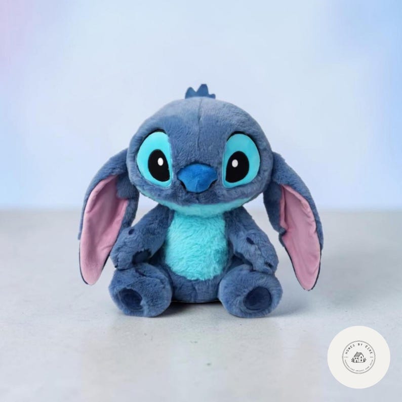 May include: A plush Stitch doll, featuring a blue body, large black eyes, and oversized ears with pink inner details. The doll has a turquoise belly and a small tuft of hair on its head. It is a soft, cuddly toy.