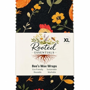 May include: A rectangular beeswax wrap with a black background featuring a floral pattern of orange and yellow flowers and green leaves. A white paper band wraps around the center with the text Rooted Essentials, Bee's Wax Wraps, and XL.