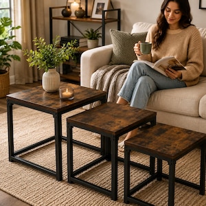 May include: A set of three nesting tables featuring square, dark brown wood-grain tops and black metal frames. The tables are arranged in a descending step pattern, with the largest table holding a white ribbed vase with greenery and a candle.