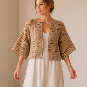 May include: A tan, open-front crochet jacket with wide, elbow-length sleeves. The jacket is made of a light, airy material and has a rectangular pattern. The jacket is worn over a light-colored dress. The overall style is casual and bohemian.