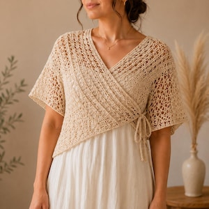 Pode incluir: Um top de crochê bege com mangas curtas e decote em V. O top tem um fecho de laço na cintura e é usado sobre um vestido branco. O padrão de crochê é aberto e arejado, criando uma textura delicada. O estilo geral é boêmio e feminino.