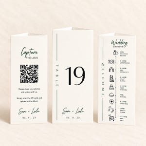 May include: Three off-white triangular table cards with black text and graphics. One card features a QR code for photo sharing, one displays the number 19, and one shows a wedding timeline with icons. All cards include the names Sam + Lulu and 05. 11. 25.