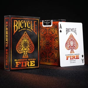 Op de afbeelding: Een kaartspel Bicycle Elements Series Fire in een zwarte doos met oranje vlam-thema schoppenafbeeldingen en tekst. Daarnaast toont een enkele witte Aas van Schoppen een bijpassend oranje vlam-schoppendesign en de tekst Fire.
