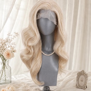 May include: A long, wavy, platinum blonde wig with a visible lace front, styled with a side part and voluminous curls that cascade down to the shoulders. The wig is displayed on a grey mannequin head wearing a simple white pearl necklace.