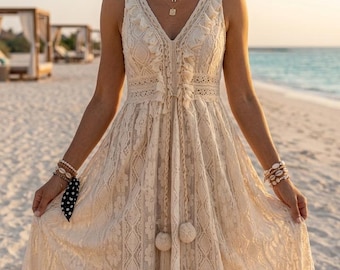 May include: Cream sleeveless lace dress with a V-neck and a flowing skirt. The dress has intricate floral and geometric patterns, with tassel details and a drawstring waist. The dress is accessorized with layered necklaces and bracelets, and a black and white polka dot scarf.