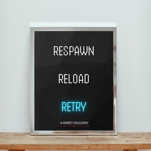 Può includere: Poster nero incorniciato con testo pixelato bianco che recita "RESPAWN", "RELOAD" e "RETRY" in blu brillante. La frase "-A GAMER'S PHILOSOPHY" è in basso. Il poster è su una superficie di legno.