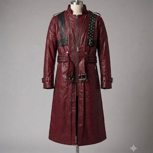 May include: A long, deep red coat with a textured finish, featuring a central zipper closure, black leather-like shoulder panels, and a studded strap detail on the left chest. The coat includes a waist belt with buckles and adjustable cuffs.