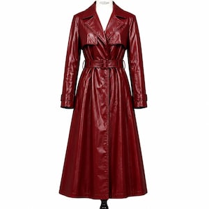 May include: A long, deep red trench coat with a glossy, patent-like finish. The coat features a wide notched collar, long sleeves with buckled cuffs, and a matching waist belt with a rectangular buckle. The design includes a storm flap detail.