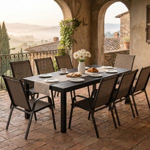May include: A rectangular black outdoor dining table with eight matching chairs featuring dark mesh fabric seats and backrests. The table is set with a light beige runner, white plates, a white vase with white daisies, and a pastry on a plate.