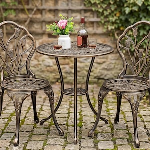 May include: A bistro set consisting of two chairs and a round table with a bronze-colored finish. The chairs feature a tulip-inspired backrest design and a lattice seat pattern. The table has a matching lattice top and a central support shelf.