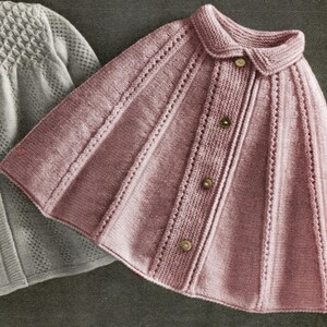 Può includere: Un mantello lavorato a maglia color rosa antico con colletto arrotondato e tre bottoni sul davanti. Il mantello presenta dettagli verticali a coste e traforati. Un capo in maglia grigia è parzialmente visibile sullo sfondo.