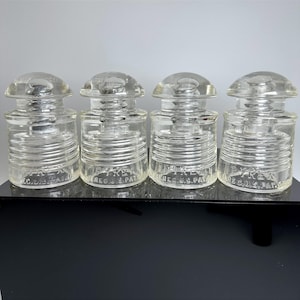 May include: Four clear glass electrical insulators with a rounded top and ribbed sides. Each piece features the embossed text PYREX REG. U.S. PAT. OFF. at the base. These vintage industrial components have a smooth, transparent finish.