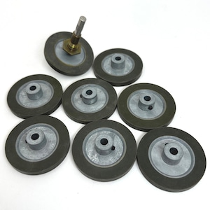 Könnte beinhalten: Eine Sammlung von acht kreisförmigen Rädern mit dunkelgrauen, gummierten Außenrändern und hellgrauen Metallzentren mit Naben. Ein Rad verfügt über eine angebrachte Metallwelle und messingfarbene Beschläge, die aus der Mitte herausragen.