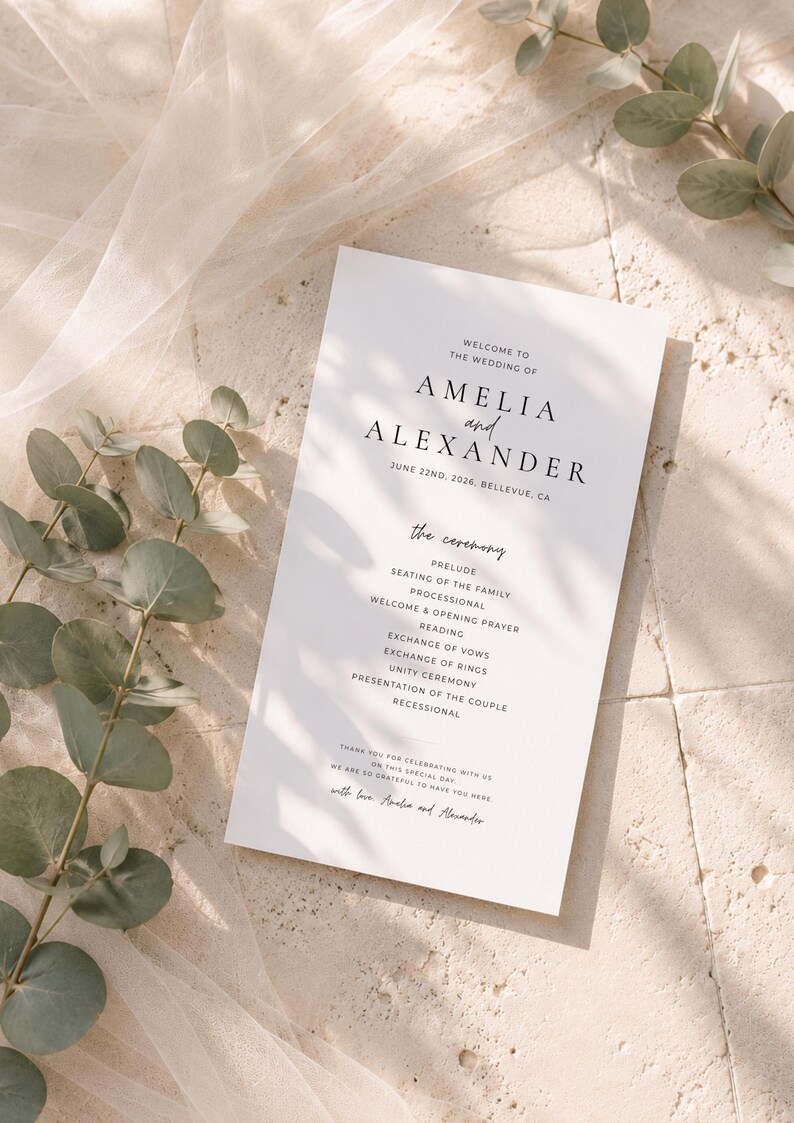 Puede incluir: Un programa de boda blanco con texto negro, con los nombres "AMELIA y ALEXANDER" y la fecha 22 de junio de 2026. El programa enumera los detalles de la ceremonia. Hojas de eucalipto y una tela transparente en el fondo.