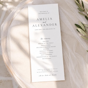 Puede incluir: Un programa de boda blanco con texto negro. El programa enumera los detalles de la boda, incluidos los nombres Amelia y Alexander, la fecha y el orden de la ceremonia. El programa est&aacute; sobre una superficie blanca.