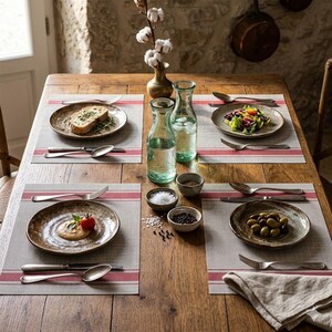 Puede incluir: Una mesa de comedor rústica preparada para una comida. Cuatro cubiertos con platos, cubiertos y manteles individuales a rayas rojas. Dos botellas de agua de vidrio, sal, pimienta y un jarrón con tallos de algodón también están sobre la mesa.