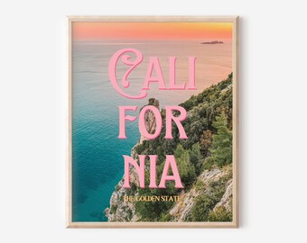 Może przedstawiać: Oprawiony wydruk przedstawiający krajobraz nadmorski z napisem "CALIFORNIA" w kolorze różowym, nad "THE GOLDEN STATE". Obraz przedstawia zachód słońca nad oceanem, ze skalistym klifem porośniętym zielenią na pierwszym planie.