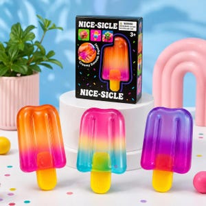 Op de afbeelding: Drie kleurrijke, ijslolly-vormige speeltjes met gele stokjes worden getoond. De speeltjes zijn in tinten van oranje, roze, blauw en paars. Een doos met de tekst "NICE-SICLE" en een ijslolly-afbeelding staat erachter.