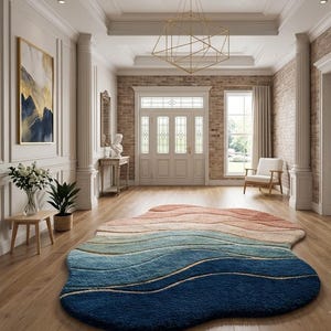 Pode incluir: Um tapete de formato orgânico irregular com um gradiente de faixas horizontais onduladas em tons de azul-marinho profundo, azul-petróleo, azul-claro, creme e pêssego suave, colocado sobre um piso de madeira clara num hall de entrada.