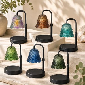 May include: Six candle warmers with black metal stands and textured glass shades in various colors including iridescent, amber, teal, light green, blue, and dark green. Each lamp features a curved arm and a circular base for holding candles.