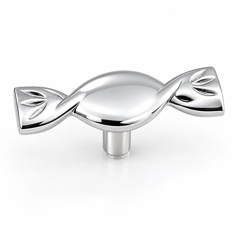 May include: A polished silver-toned metal cabinet knob shaped like a wrapped candy. The central body is smooth and rounded, while the two flared ends feature a subtle engraved leaf-like pattern. A single cylindrical post extends from the center.