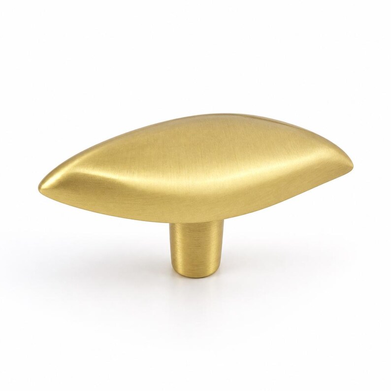 May include: A gold-toned metal cabinet knob featuring a smooth, elongated, leaf-like shape with a brushed finish. The hardware has a central cylindrical base that connects to the wider, tapered top section, creating a sleek and uniform appearance.