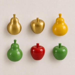 May include: A set of six decorative fruit-shaped objects arranged in two rows. The top row features a metallic gold pear, a metallic gold apple, and a bright yellow pear. The bottom row includes a glossy green pear, a glossy red apple, and a glossy green apple.