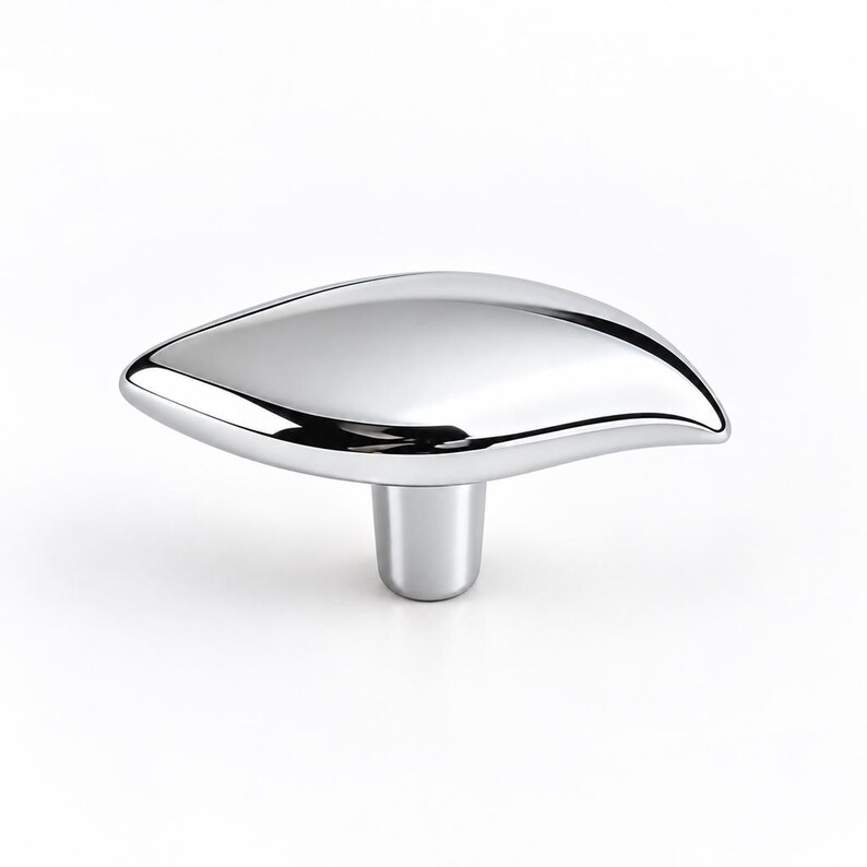 May include: A polished chrome cabinet knob featuring a smooth, elongated, leaf-like shape that tapers to a point on one side. The hardware has a reflective, mirror-like finish and a cylindrical base that connects to the main body of the knob.