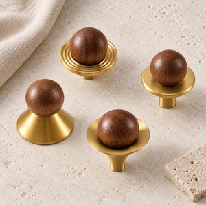 May include: Four cabinet knobs featuring spherical dark brown wooden tops set onto circular brushed gold metal bases. Each knob has a distinct base shape, including tiered rings, a smooth conical form, and a flat disc, showcasing wood grain textures.