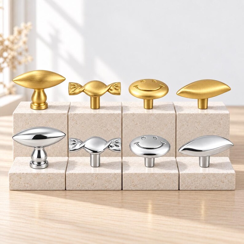 May include: A collection of eight cabinet knobs arranged in two rows. The top row features four gold-toned knobs in leaf, candy, smiley face, and petal shapes. The bottom row displays four matching silver-toned knobs in the same four distinct designs.