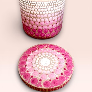 Peut inclure: Un récipient cylindrique et un couvercle circulaire ornés d'un motif mandala peint à la main avec des points dans des tons de blanc, rose clair et magenta foncé. Le motif passe du blanc au sommet au rose profond à la base. Texte Spring Dots.