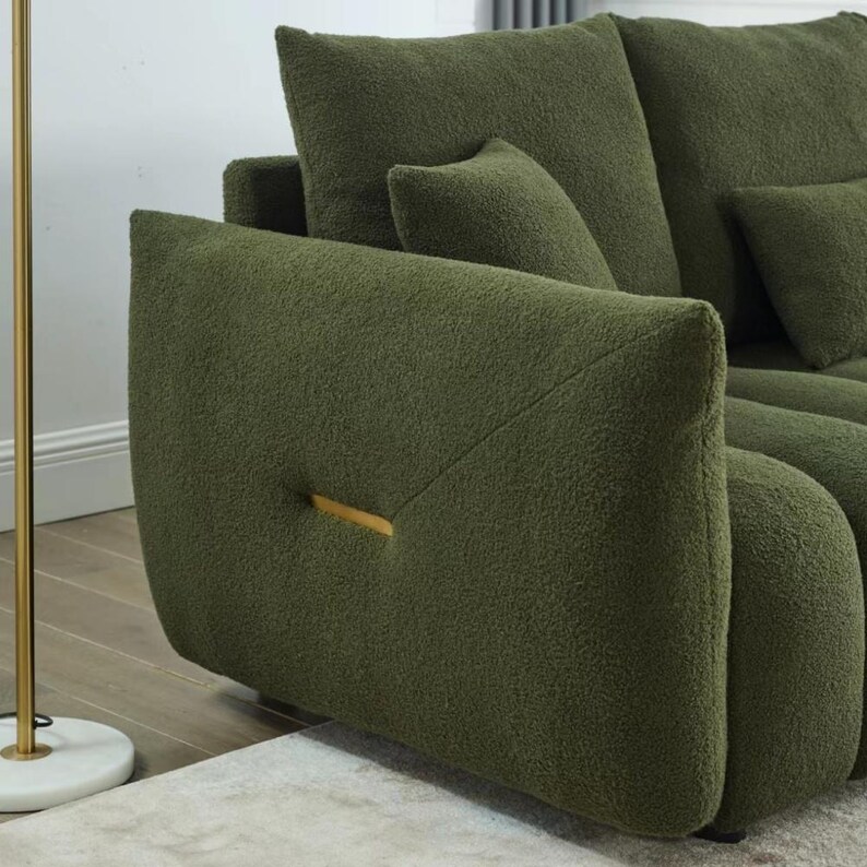 Puede incluir: Sof&aacute; boucl&eacute; verde oliva con cojines a juego. El sof&aacute; presenta un dise&ntilde;o moderno con un acento dorado en el reposabrazos. La textura afelpada y el color crean una est&eacute;tica acogedora y atractiva.