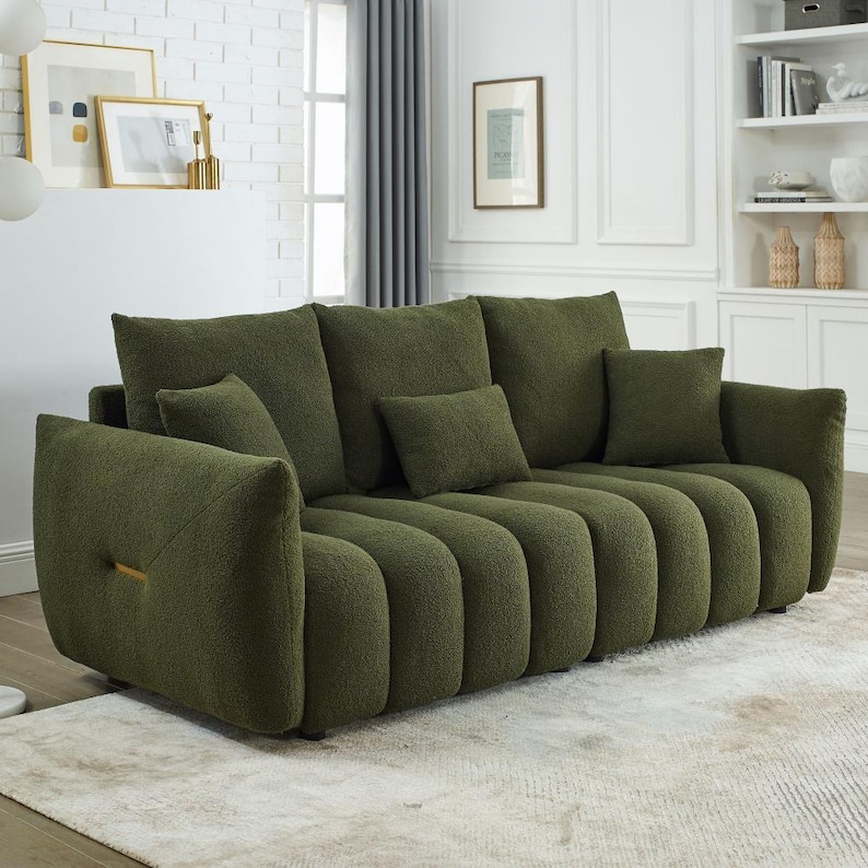 Puede incluir: Un sof&aacute; verde oliva con un dise&ntilde;o acanalado &uacute;nico. El sof&aacute; tiene varias almohadas a juego y un detalle dorado en el brazo. El sof&aacute; est&aacute; colocado sobre una alfombra clara en una habitaci&oacute;n luminosa.
