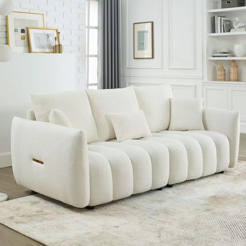 Puede incluir: Un sof&aacute; grande, de color blanco roto, con un dise&ntilde;o redondeado &uacute;nico. El sof&aacute; tiene m&uacute;ltiples cojines y una tela texturizada. Los brazos tienen una forma distintiva y la pieza se asienta sobre una alfombra de color neutro. Los cojines decorativos a&ntilde;aden comodidad.