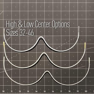 May include: Three silver-colored metal underwire bra components with high and low center options, labeled with the text High & Low Center Options Sizes 32-46. The wires are arranged vertically against a black grid background with white markings.