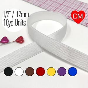 May include: A white elastic band measuring 1/2 inch in width, presented in 10-yard units. The image includes a ruler, two heart-shaped pins, and a color palette showing black, white, brown, red, yellow, purple, and blue options.
