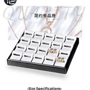 May include: A black jewelry display tray with white inserts, holding two pairs of gold earrings. The tray has the text "TAIIE" and "QUALITY" in the background. The text "-Size Specifications-" is also visible.