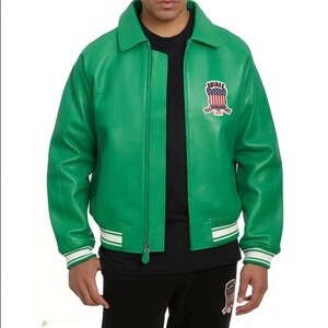 Puede incluir: Chaqueta de cuero verde brillante con cremallera, cuello y parche en el pecho. La chaqueta tiene pu&ntilde;os y dobladillo a rayas blancas y verdes. La chaqueta se usa sobre una camiseta negra. Estilo bomber cl&aacute;sico.