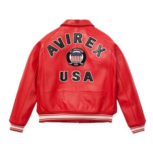May include: A red leather bomber jacket with the word "AVIREX" arched across the shoulders. Below the word "AVIREX" is a circular patch with the words "ALL AMERICANS ESTABLISHED 1975" and the word "USA" below the patch. The jacket has a white and red striped trim.