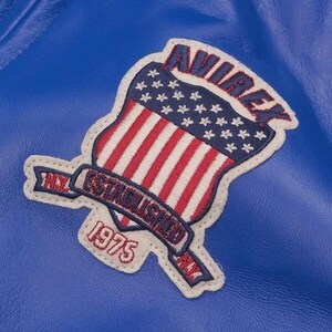 May include: Close-up of a blue leather jacket featuring a patch with the word "AVIREX" in red, above a shield design of the American flag. The patch also includes the text "ESTABLISHED 1975" and "NY".