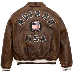Może przedstawiać: Brązowa sk&oacute;rzana kurtka z napisem "AVIREX" w białych literach na plecach. Poniżej naszywka z napisem "ALL AMERICANS ESTABLISHED 1975" i flagą USA. Poniżej napis "USA". D&oacute;ł kurtki w biało-czarne paski.
