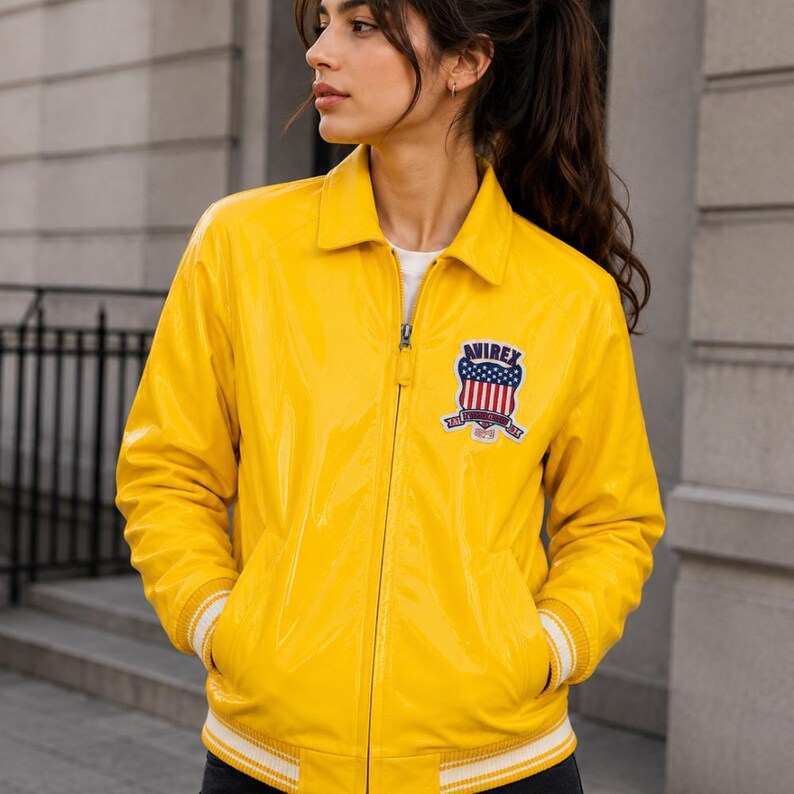 May include: Bright yellow jacket with a zip-up front, collar, and white striped cuffs. The jacket features a patch on the chest with the text "AVIREX" and a design of stars and stripes. The jacket is a classic style.