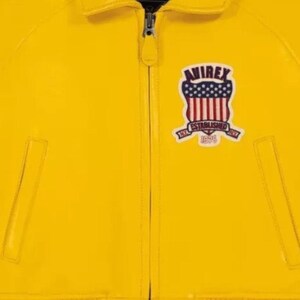 May include: Close-up of a bright yellow jacket with a zipper closure. The jacket features a patch with the text "AVIREX" above a design of red and white stripes and blue stars. The patch also includes the text "ESTABLISHED 1975".