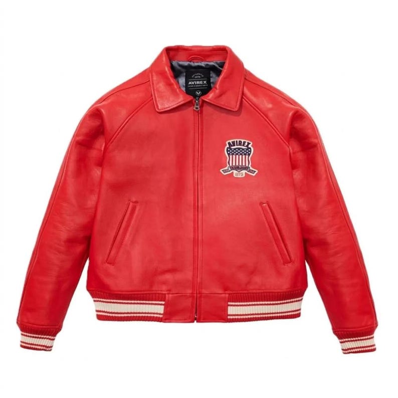 May include: A bright red leather jacket with a collared neckline and a zipper closure. The jacket features a patch on the chest with the text "AVIREX" and a design of the American flag. The cuffs and hem have white and red striped detailing.