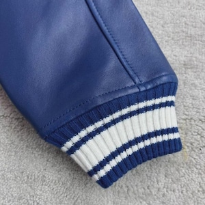 May include: Close-up of a blue leather jacket sleeve. The cuff is ribbed with alternating stripes of white and blue. The jacket's leather has a smooth texture.