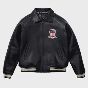 Puede incluir: Chaqueta de cuero negra de estilo bomber. Presenta cuello, cierre de cremallera y pu&ntilde;os y dobladillo acanalados con rayas blancas. Un parche bordado en el pecho muestra el nombre de la marca e im&aacute;genes patri&oacute;ticas.