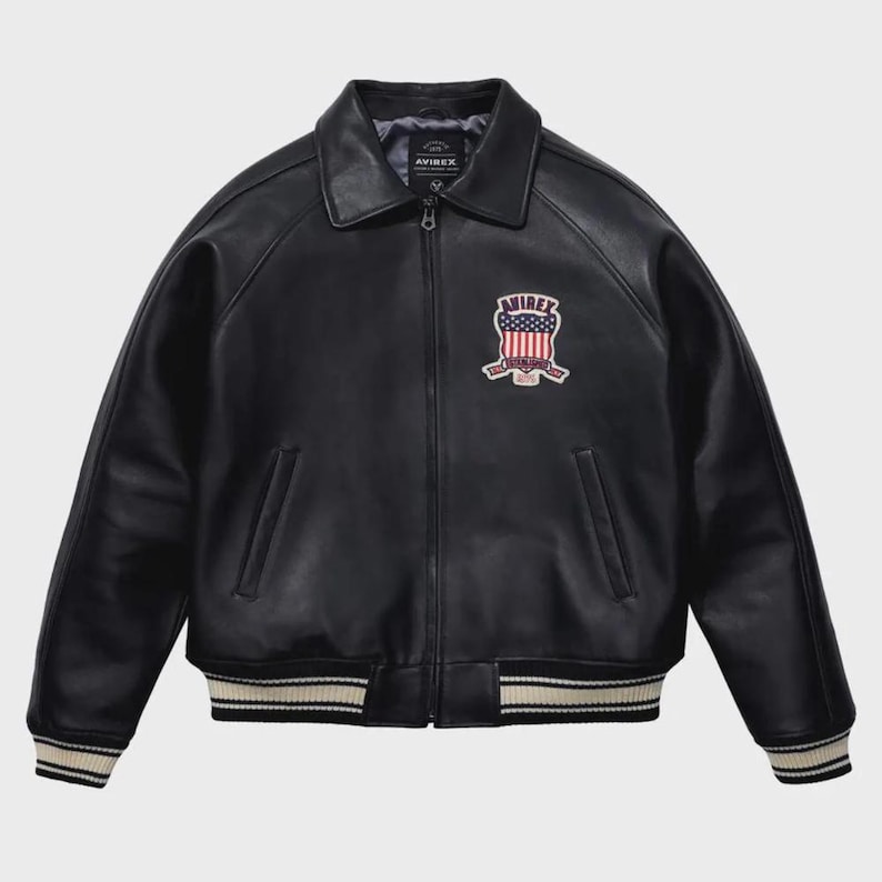 Puede incluir: Chaqueta de cuero negra de estilo bomber. Presenta cuello, cierre de cremallera y pu&ntilde;os y dobladillo acanalados con rayas blancas. Un parche bordado en el pecho muestra el nombre de la marca e im&aacute;genes patri&oacute;ticas.