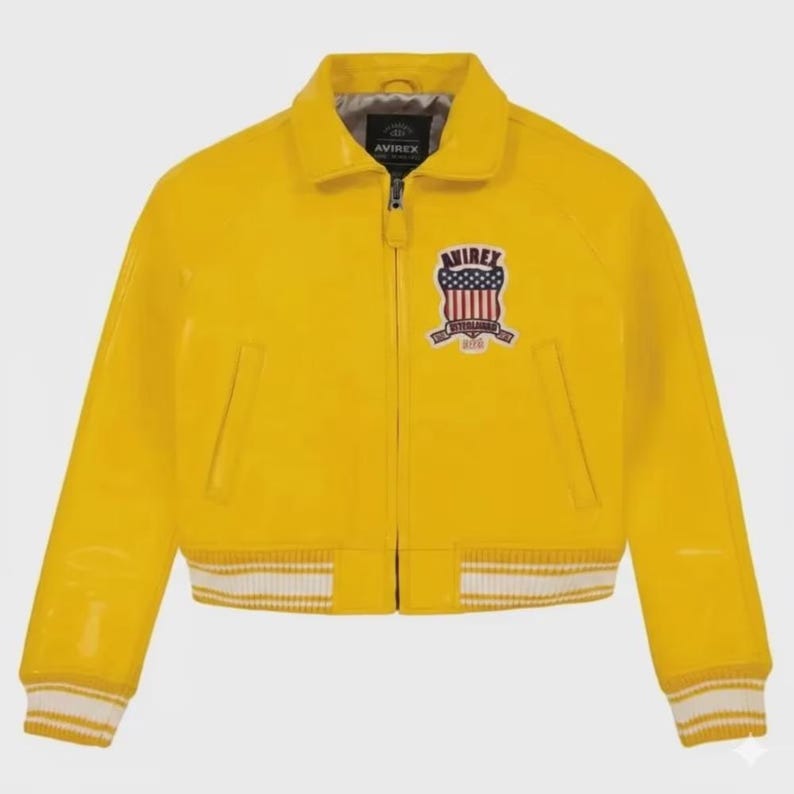 May include: A bright yellow bomber jacket with a glossy finish. The jacket features a zip-up front, a collar, and white and yellow striped cuffs and hem. An embroidered patch with a shield design and the word "AVIREX" is on the chest.